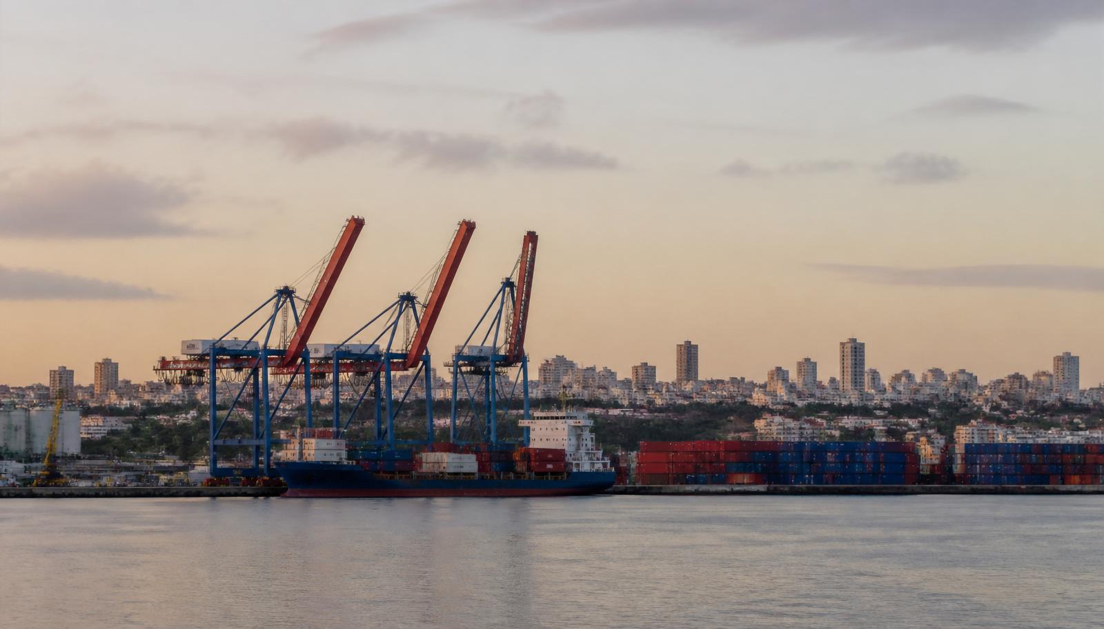 Porto de Salvador ao amanhecer visto de longe, com guindastes portuários, contêineres empilhados em vermelho e azul e navio cargueiro atracado, com a cidade ao fundo