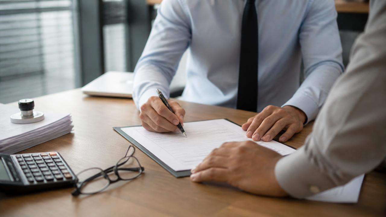 Corretor de seguros e empresário do setor de construção assinando apólice de seguro garantia sobre mesa de escritório com calculadora e documentos carimbados
