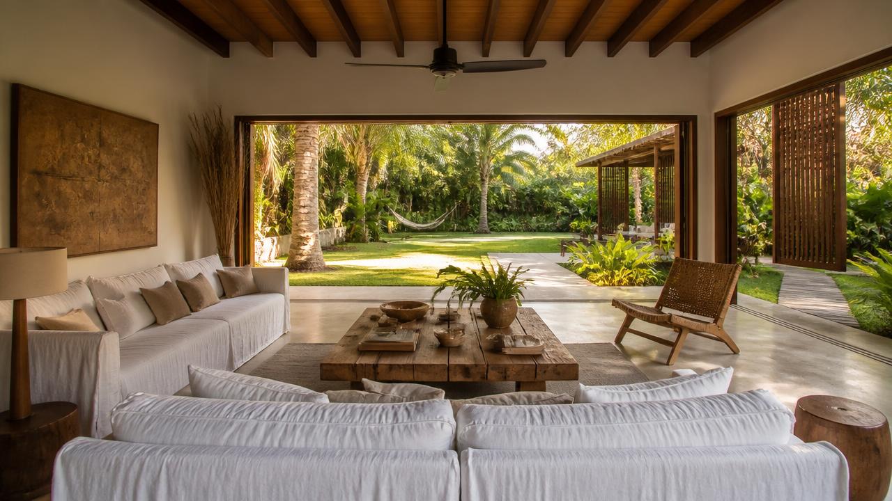 Sala de estar integrada ao jardim de villa de alto padrão no litoral sul da Bahia, com mobiliário de madeira maciça, sofás de linho claro e vista para palmeiras